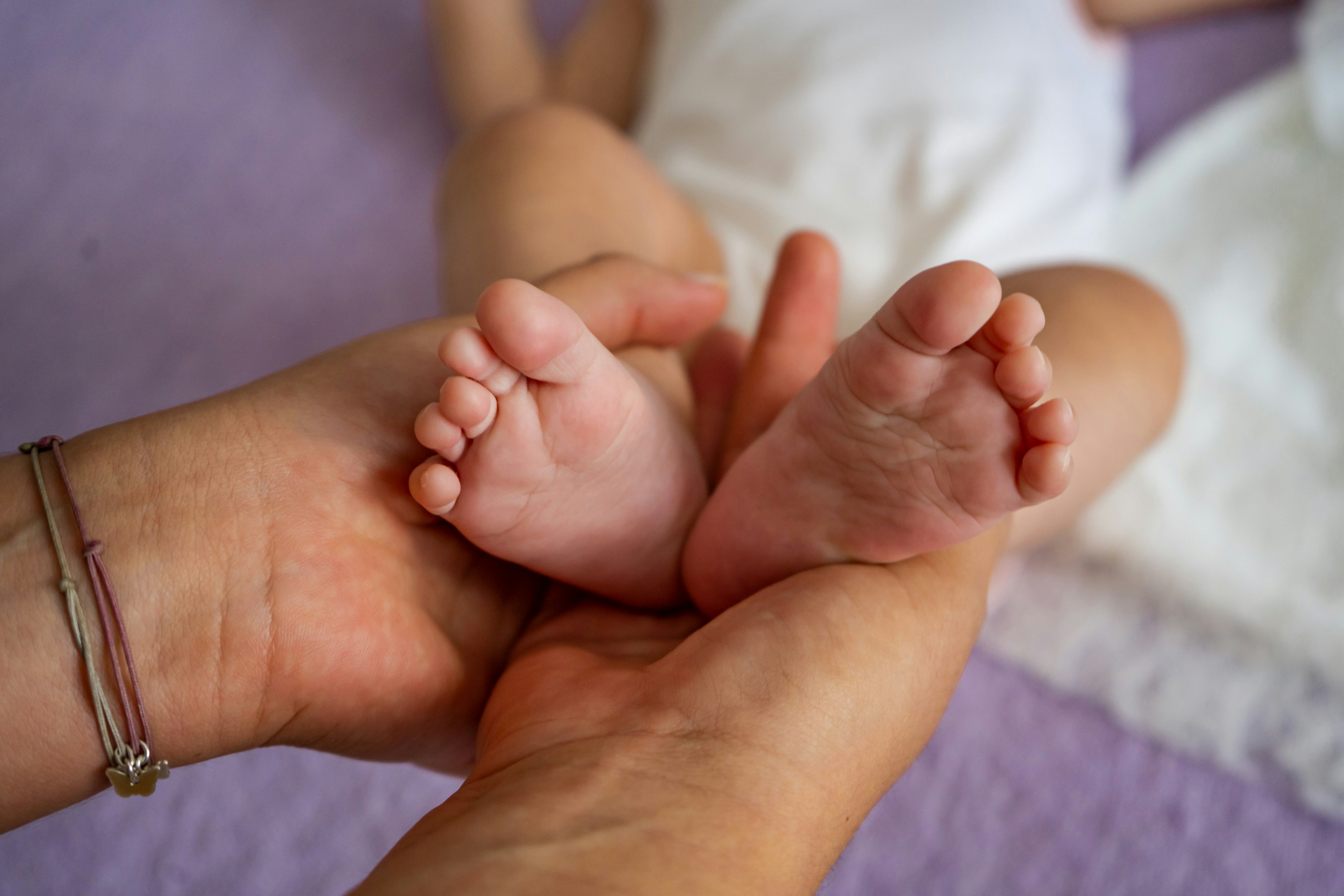 A caregiver gently holding a newborn's feet, showcasing a nurturing connection on a soft purple surface.