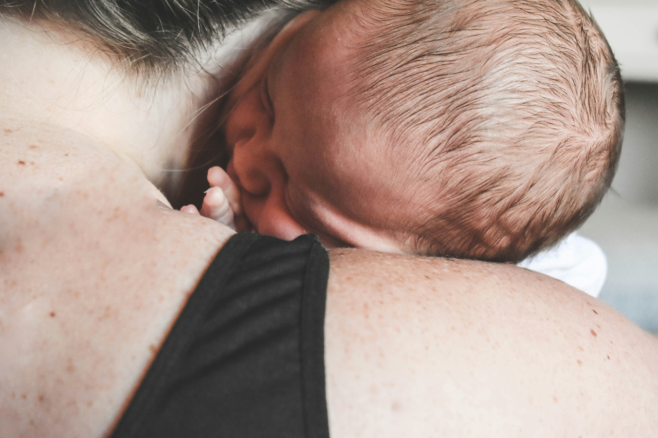 A close-up image of a newborn baby nestled against a parent's shoulder, depicting a moment of tenderness and connection.